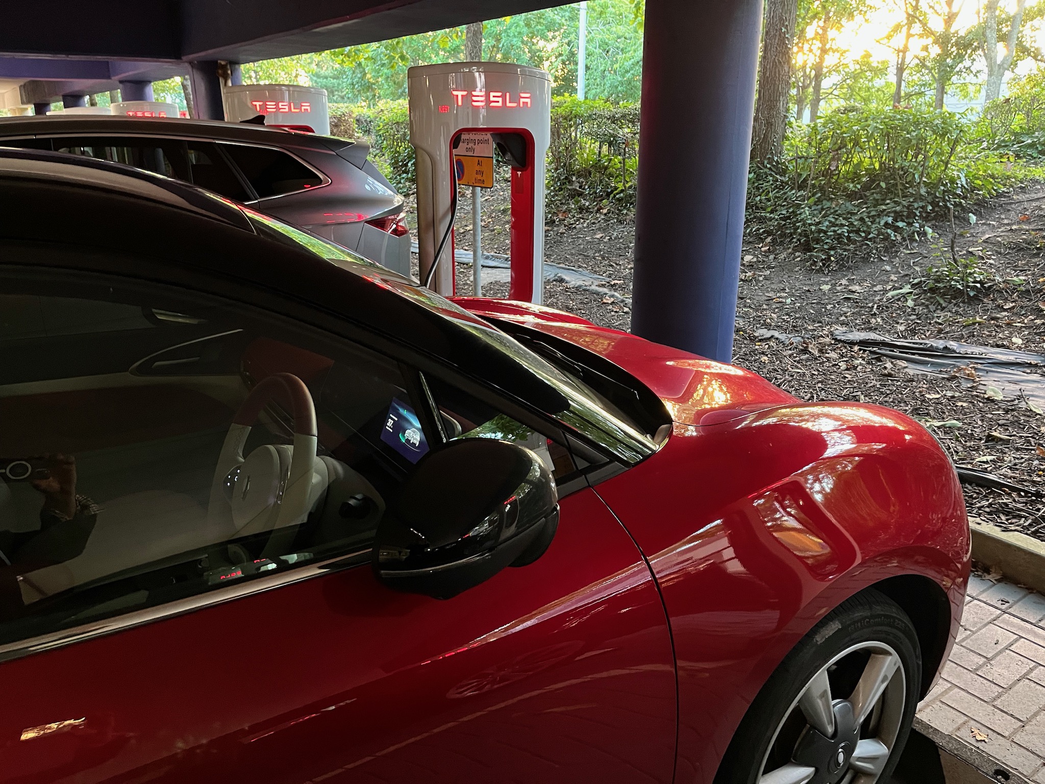red car next to Tesla charger in a car park